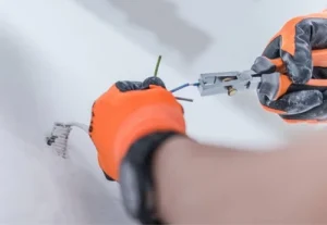 close up of an electricians hands wearing orange protective gloves and using electrical pliers to install new electrical wiring